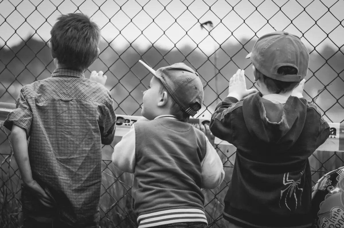 Tre bambini dietro una rete parlano con altri bambini che sono dall'altra parte