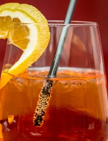 Bicchiere di Aperol Spritz con ghiaccio, fetta di arancia e cannuccia metallica, classico aperitivo italiano servito fresco