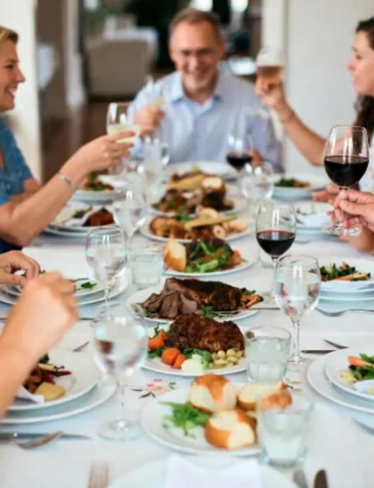 Cena conviviale in home restaurant con ospiti che brindano intorno a un tavolo ricco di piatti italiani, arrosti, verdure e calici di vino.