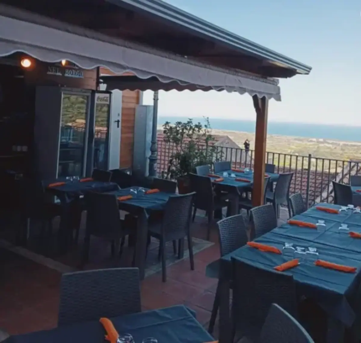 Terrazza panoramica del ristorante Sapori nel Borgo con tavoli apparecchiati e vista mozzafiato sul mare al tramonto.