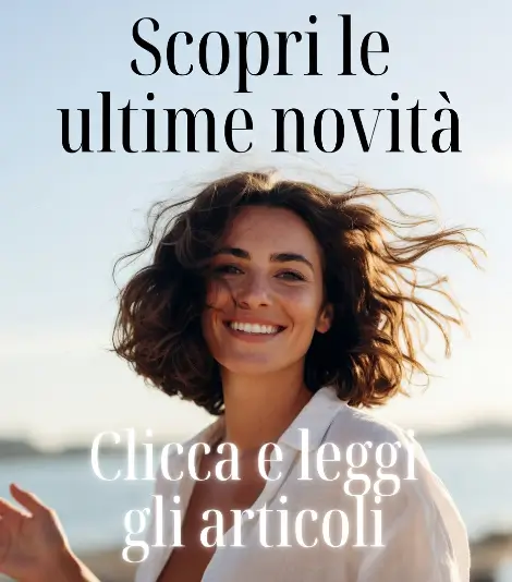 Donna sorridente con capelli castani mossi dal vento sulla spiaggia, che guarda verso la macchina fotografica con espressione felice e naturale.