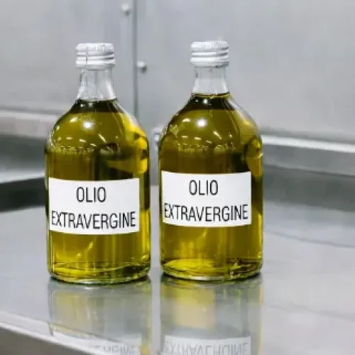 Due bottiglie di olio extravergine di oliva italiano su banco inox in ambiente di produzione – prodotto tipico made in Italy