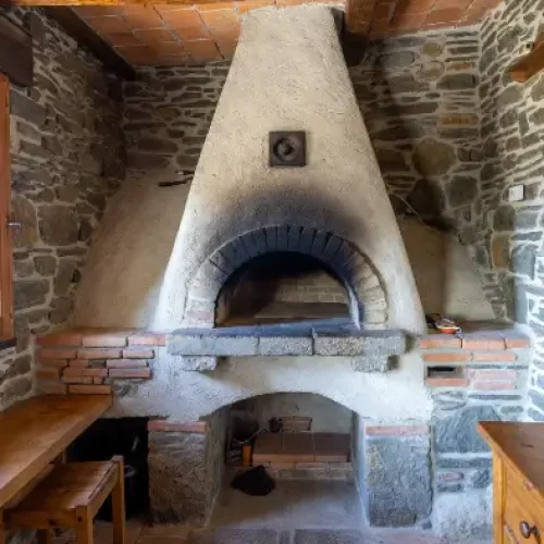 Interno rustico di una casa tradizionale con antico forno a pietra refrattaria integrato nella parete, bocca del forno spenta.