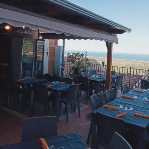 Terrazza panoramica del ristorante Sapori nel Borgo con tavoli apparecchiati e vista mozzafiato sul mare al tramonto.
